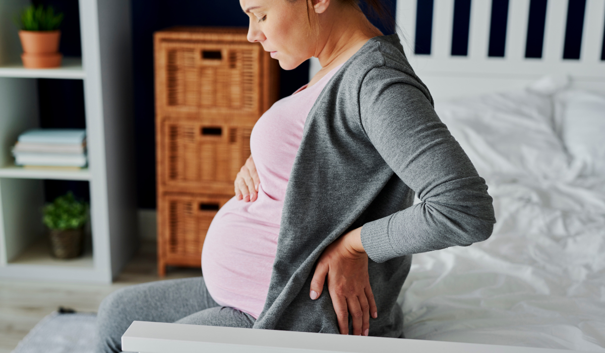 pregnant woman sitting on bed holding her back