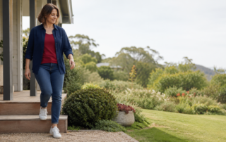 Middle-aged woman confidently stepping down from a low garden step outside a home, with relaxed posture, lush greenery and open space beside her.